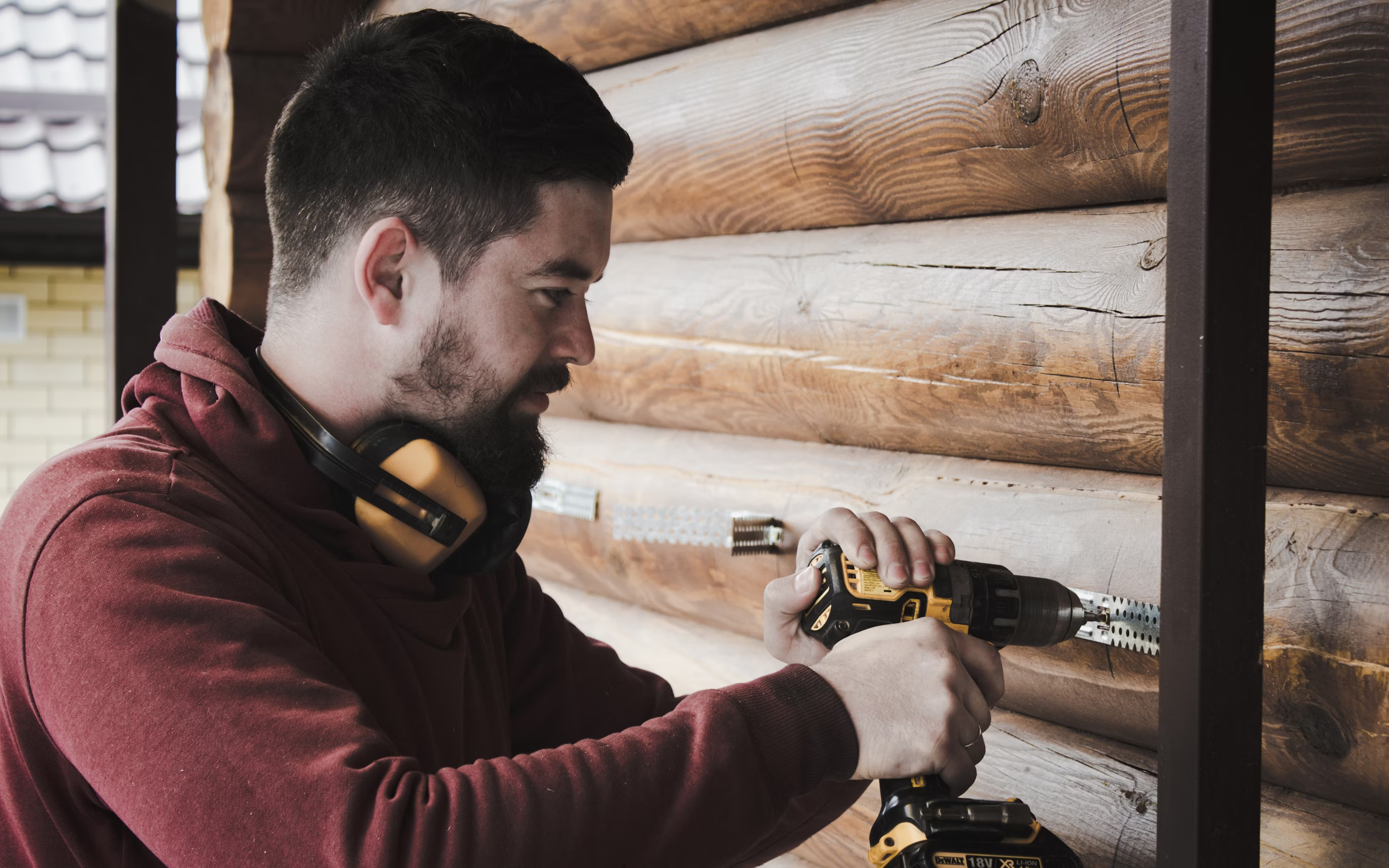 Contractor wearing a black beanie and safety gear working on a renovation project in a dimly lit space with wooden beams visible
