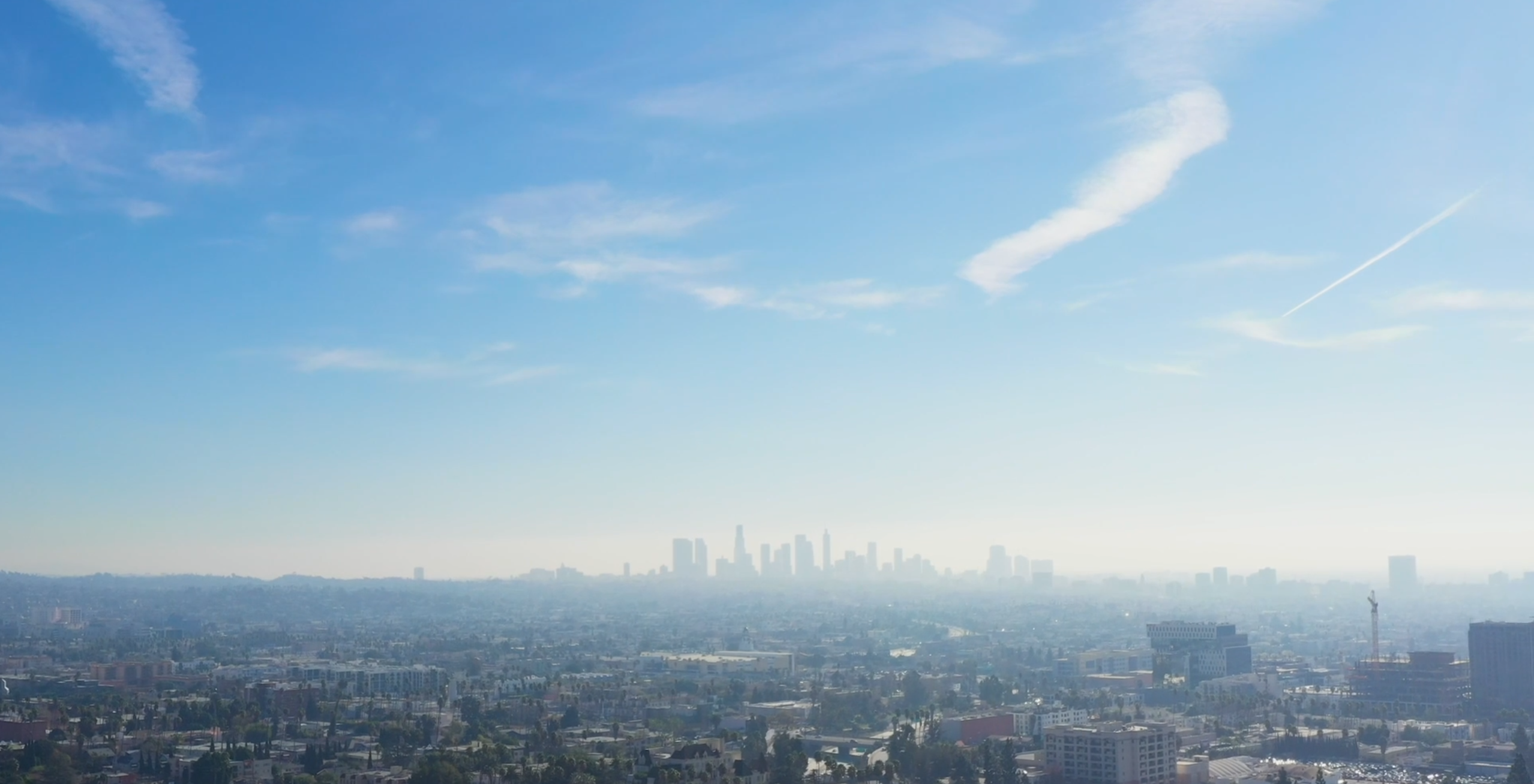 Aerial view of downtown Los Angeles skyline with skyscrapers against a blue sky and mountains in the background