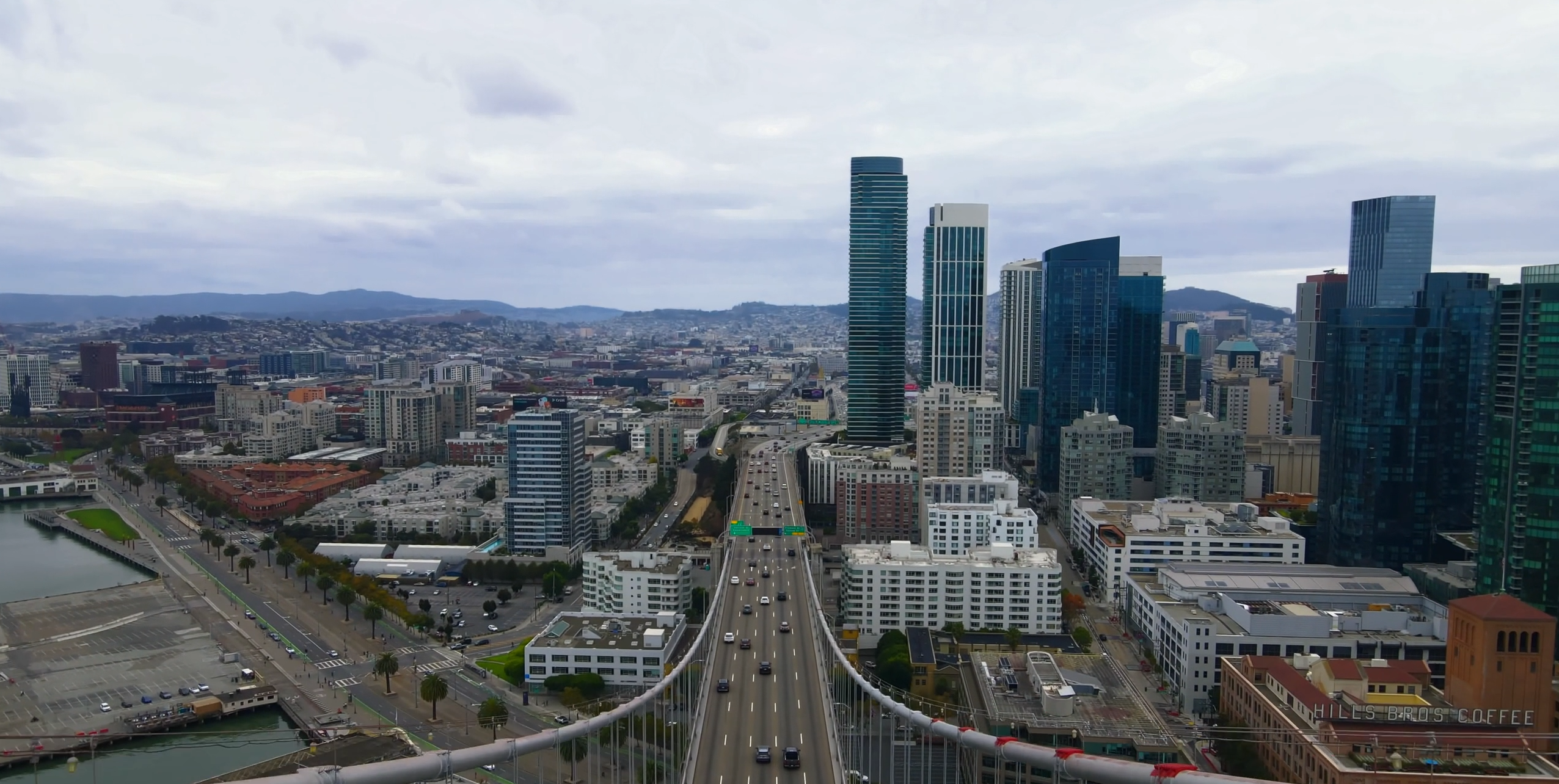 Aerial view of downtown San Francisco skyline with iconic skyscrapers and the Bay Bridge visible against a cloudy sky